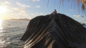 Una persona sentada sobre una roca grande junto al mar al atardecer.