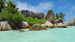 Una playa tropical con grandes rocas, agua turquesa cristalina y abundante vegetación.