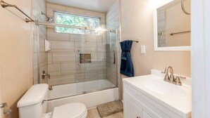 Casa de banho moderna com cabine de duche em vidro, sanita branca e toucador com lavatório.