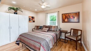 A bedroom with a bed, a chair, a small table, a ceiling fan, a window, and a painting on the wall. - Near Downtown Waxhaw Mellow Yellow Suite A  (Waxhaw)
