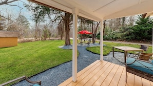 A covered patio area with a wooden deck, outdoor seating, and a view of a well-maintained lawn and trees. - Near Downtown Waxhaw Mellow Yellow Suite A  (Waxhaw)