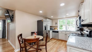 A modern kitchen with white cabinets, a granite countertop, and a dining area with wooden chairs. - Near Downtown Waxhaw Mellow Yellow Suite A  (Waxhaw)