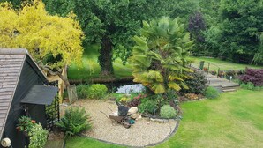A garden with a pond, various plants, and a wooden deck.