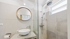 A bathroom with a round mirror, a white sink, a shower, and a window.