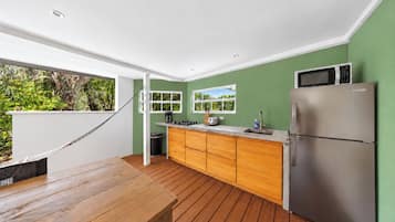 Une cuisine moderne avec une table en bois, un réfrigérateur en acier inoxydable et une vue sur la verdure à l’extérieur.