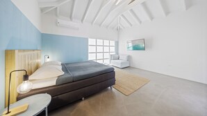 A modern bedroom with a bed, bedside lamp, and a view of the outdoors.