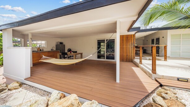 A modern house with a wooden deck, a hammock, a kitchen, and a dining area.