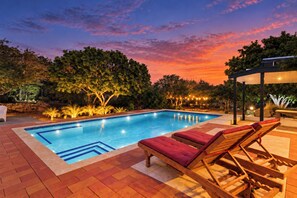A swimming pool with a tiled edge, surrounded by a brick patio. There are wooden lounge chairs with red cushions. - Unique experience in the nature of Aruba #2 (Paradera)