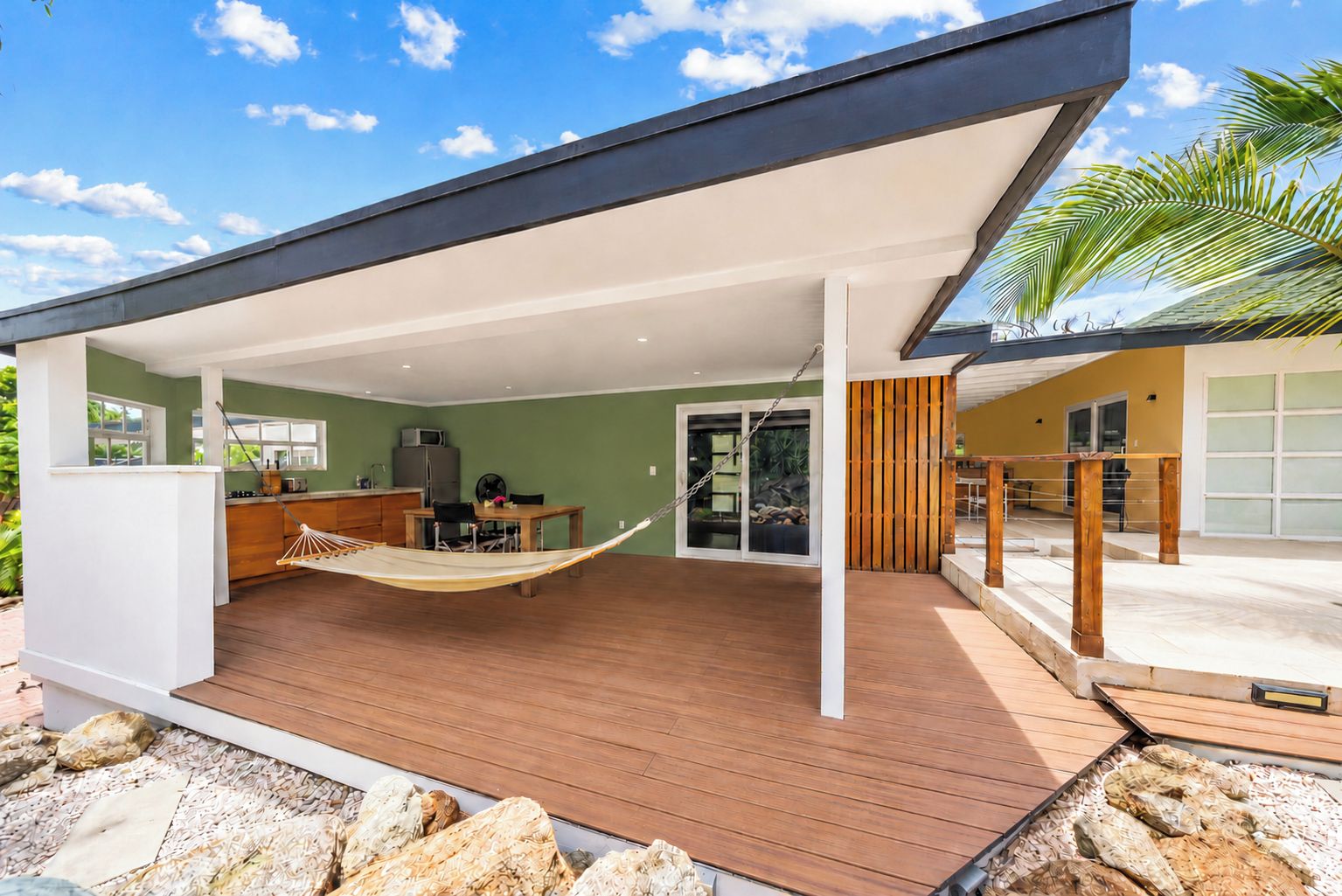 Une maison moderne dotée d’un patio couvert, d’un hamac, d’un coin repas et d’un garage.