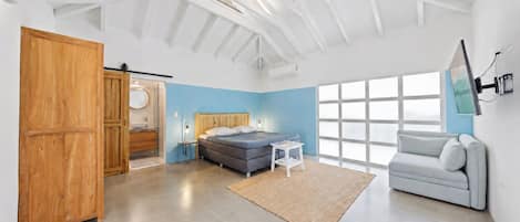 Une chambre moderne avec un lit, un canapé, une grande fenêtre et une armoire en bois.