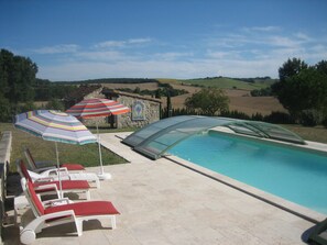 A swimming pool with lounge chairs and umbrellas, surrounded by a stone building and a view of rolling hills. - LE Calme Dans UN Ecrin DE Verdure (POUPAS)