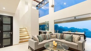 A modern living room with a large sectional sofa, a glass coffee table, and a view of the sea.