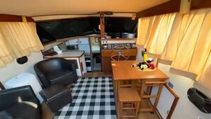A compact kitchen with a stove, sink, and a wheel for steering. There is a dining area with a table and chairs, and a checkered floor.