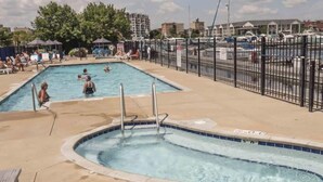 A swimming pool area with a hot tub, lounge chairs, and a fenced parking area.