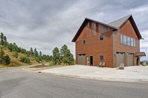 A two-story building with a large garage, a covered outdoor seating area, and a view of a winding road and forested hillside. - Game room, fully paved roads, WiFi and luxury finishes (Lead)
