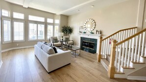 A spacious living room with a large sofa, a fireplace, and a staircase. - Panoramic ocean view and stunning sunsets in Oceanside with EV charger & AC! (Oceanside)