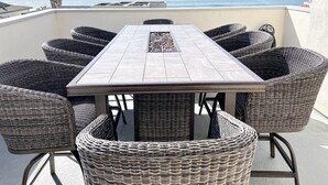 A patio with a table and wicker chairs, overlooking a body of water. - Panoramic ocean view and stunning sunsets in Oceanside with EV charger & AC! (Oceanside)