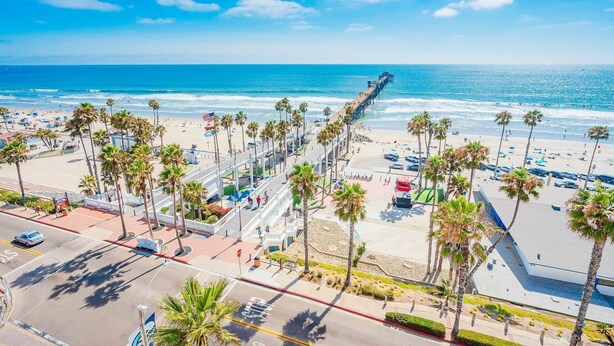 A beach with a long pier extending into the ocean, palm trees lining the promenade, and a clear blue sky. - Panoramic ocean view and stunning sunsets in Oceanside with EV charger & AC! (Oceanside)