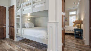 A bedroom with a bunk bed, wooden flooring, a bedside table with a lamp, and a window with blinds. - Destin- Miramar Beach Area- Seas the Day Stunning home with ocean views (Destin)