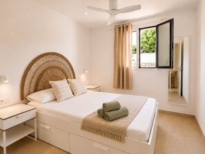 Ein Schlafzimmer mit einem Bett, Nachttischen, einem Deckenventilator, einem Fenster mit Vorhängen und einem Spiegel.