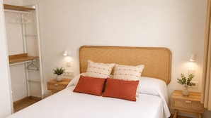 A bedroom with a bed, two bedside tables, a bedside lamp, a closet, and a wall-mounted shelf. - Beautiful house near the beach of Punta Prima (Punta prima)