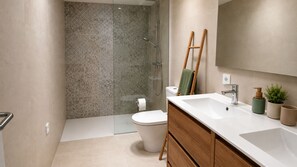 Un baño moderno con ducha, inodoro y tocador con lavamanos y espejo.