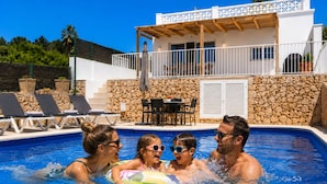 A swimming pool with lounge chairs, a stone wall, and a wooden deck. - Beautiful house near the beach of Punta Prima (Punta prima)