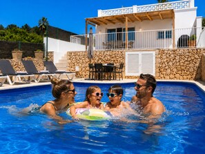 Una piscina con sillas de descanso, un muro de piedra y una terraza de madera.