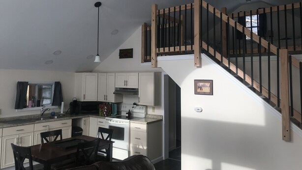 Une cuisine moderne avec des meubles blancs, un coin repas avec une table et des chaises en bois foncé, et un escalier avec des rampes en bois menant à l’étage supérieur.
