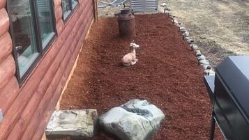 A wooden deck with a red mulch area, a grill, and a small statue.