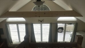 Une pièce avec un plafond en pente, un ventilateur de plafond et deux fenêtres avec des rideaux.