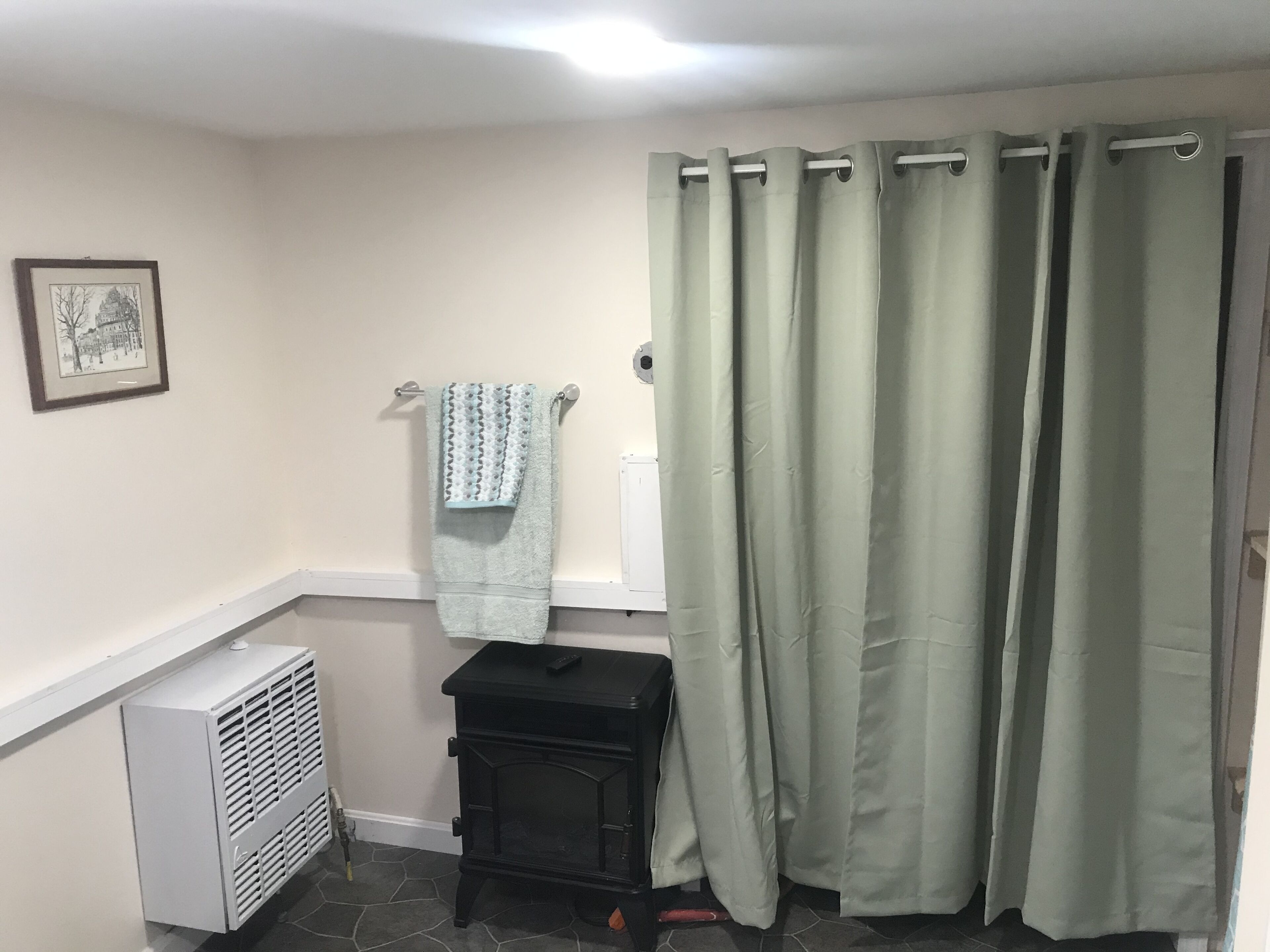 A bathroom with a white radiator, a black heater, a towel on a rack, and a green shower curtain.