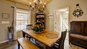 A dining area with a wooden table, benches, a chandelier, and a bookshelf with decorative items. - Quiet Cabin Mountain Retreat UC STR #021754 (Blairsville)