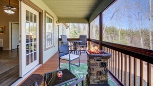 A covered porch with a stone fire pit, outdoor seating, and a view of trees. - Quiet Cabin Mountain Retreat UC STR #021754 (Blairsville)