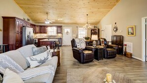 A spacious living room with a high wooden ceiling, a fireplace, leather chairs, a sofa, and a kitchen in the background. - Quiet Cabin Mountain Retreat UC STR #021754 (Blairsville)
