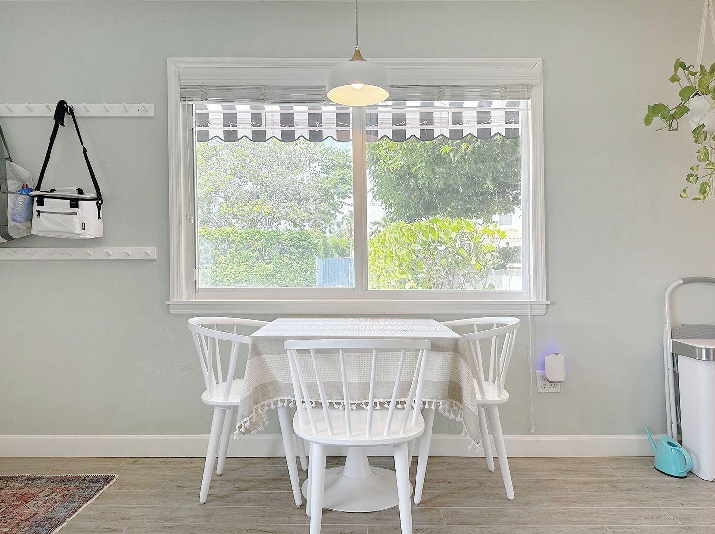 A dining area with a white table and chairs, a window with a checkered valance, and a hanging bag.