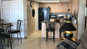 A modern kitchen with a refrigerator, microwave, and stove. There is a dining area with chairs and a table. - Ground floor Condo - No need for elevators - Steps away to the beach and pool. (Murrells Inlet)