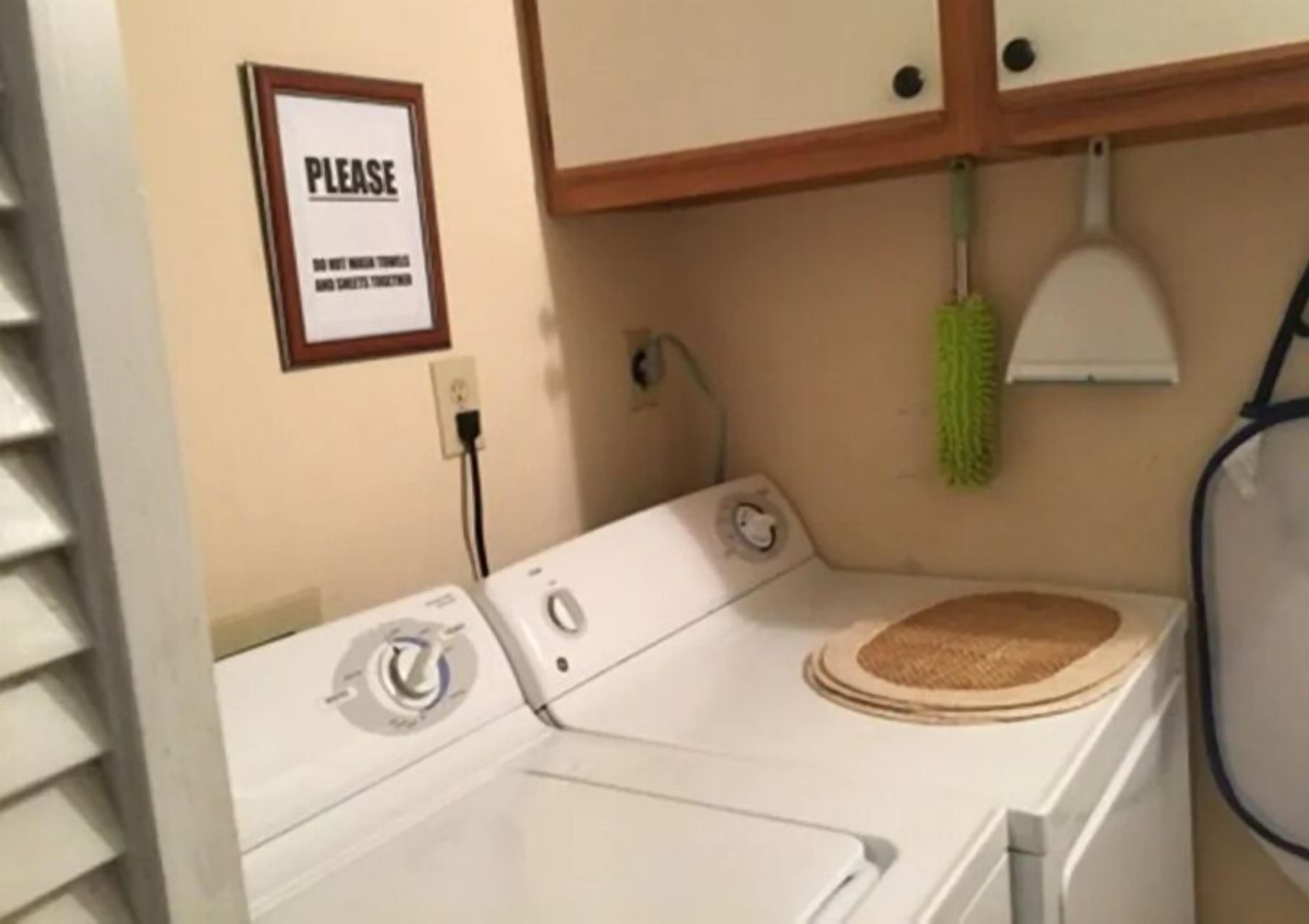 A laundry area with a washing machine, a sign on the wall, and a green mop hanging on the wall.