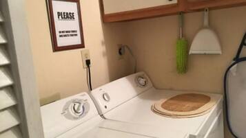 A laundry area with a washing machine, a sign on the wall, and a green mop hanging on the wall.