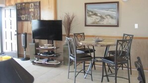 A dining area with a table and chairs, a television on a stand, and a framed picture on the wall. - Ground floor Condo - No need for elevators - Steps away to the beach and pool. (Murrells Inlet)