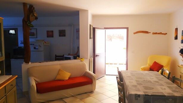 Un salón con un sofá, una mesa de comedor y una silla. Hay una puerta que da a otra habitación y una ventana con vistas al exterior.