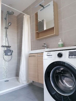 Enjoy a refreshing shower with a rain showerhead and convenient washing machine in this bathroom.