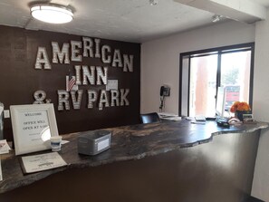 Ein Empfangstisch mit einem Schild, auf dem 'AMERICAN INN RV PARK' steht, und ein Willkommensschild, das anzeigt, dass das Büro um 16:00 Uhr öffnet.