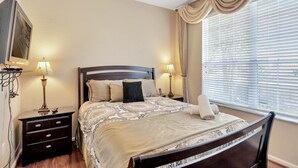 Un dormitorio ordenado con cama, dos mesitas de noche, una lámpara y una ventana con persianas.