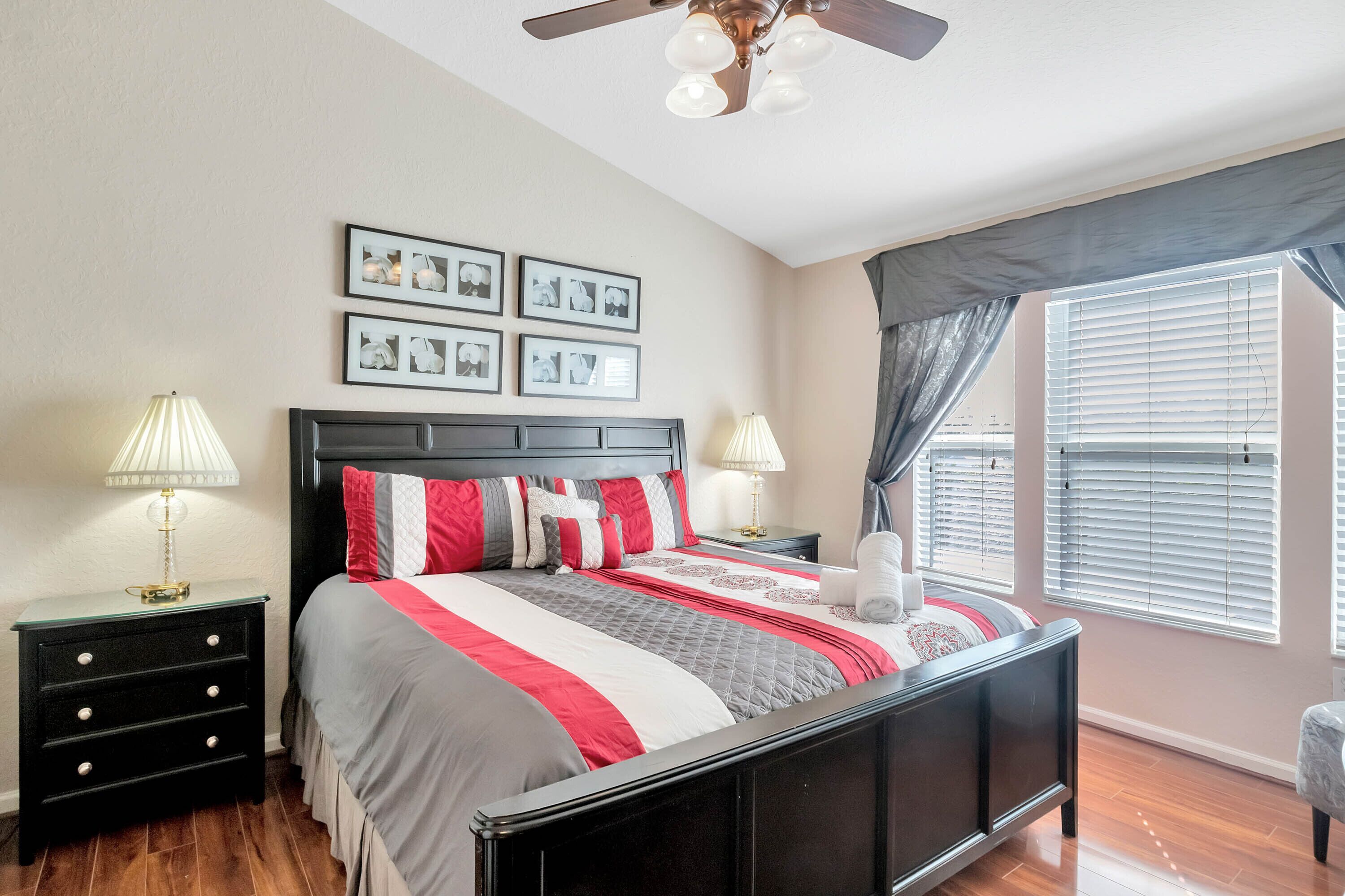 A bedroom with a bed, nightstands, lamps, a ceiling fan, and framed pictures on the wall.