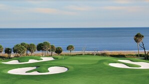 A golf course with sand bunkers, palm trees, and a view of the ocean. - Renovated Oceanfront Resort and oceanview condo - 3521 Villamare (Hilton Head Island)