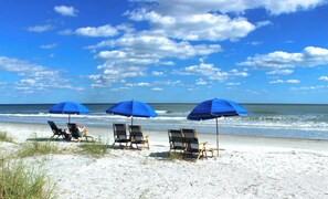 Una playa con tres sombrillas azules y sillas de playa.