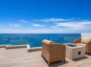 Un balcone con mobili in vimini, una ringhiera in vetro e vista sull'oceano.