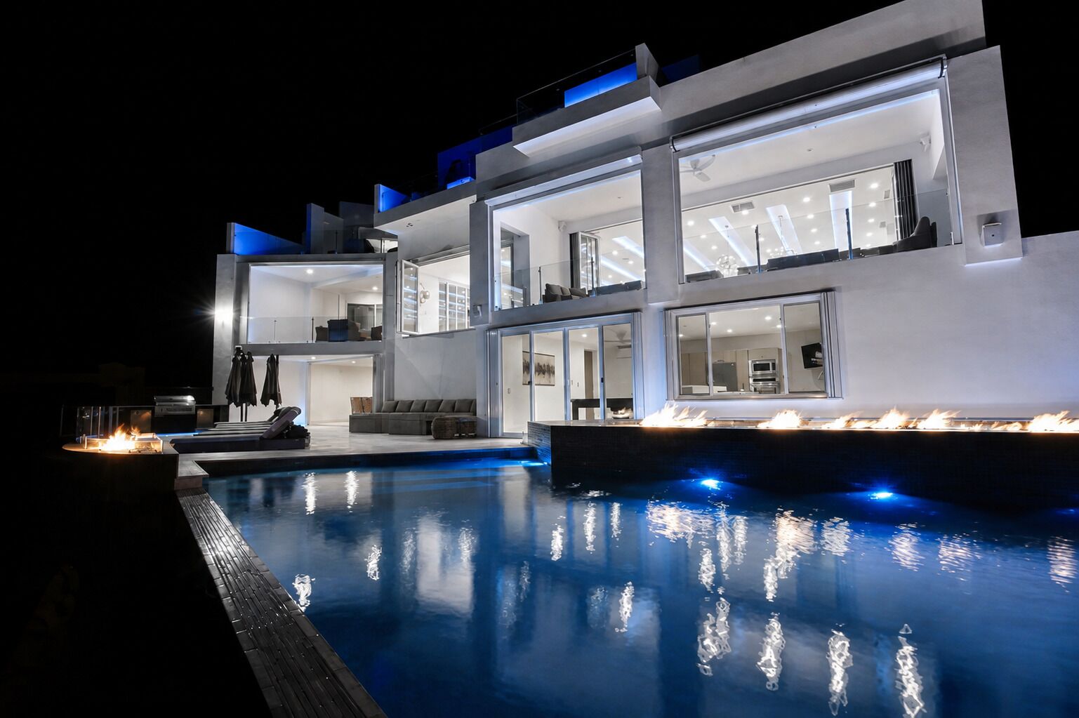 Een modern meerlaags huis met een zwembad, buitenmeubilair en een goed verlicht interieur.