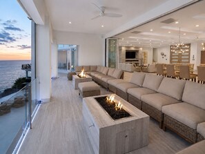 Ein modernes Wohnzimmer mit einer großen Eckcouch, einem Kamin und einem Balkon mit Meerblick.